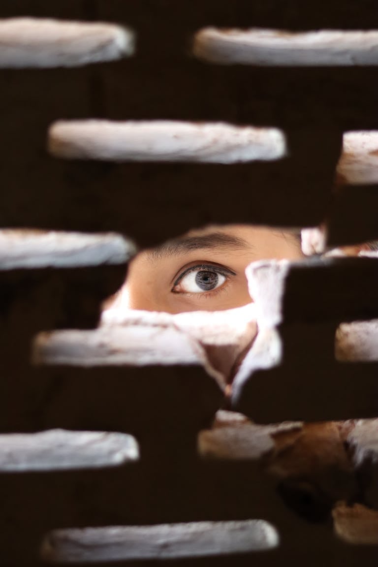 A mysterious eye peeks through a small gap in a brick wall, creating an intriguing and intense visual.