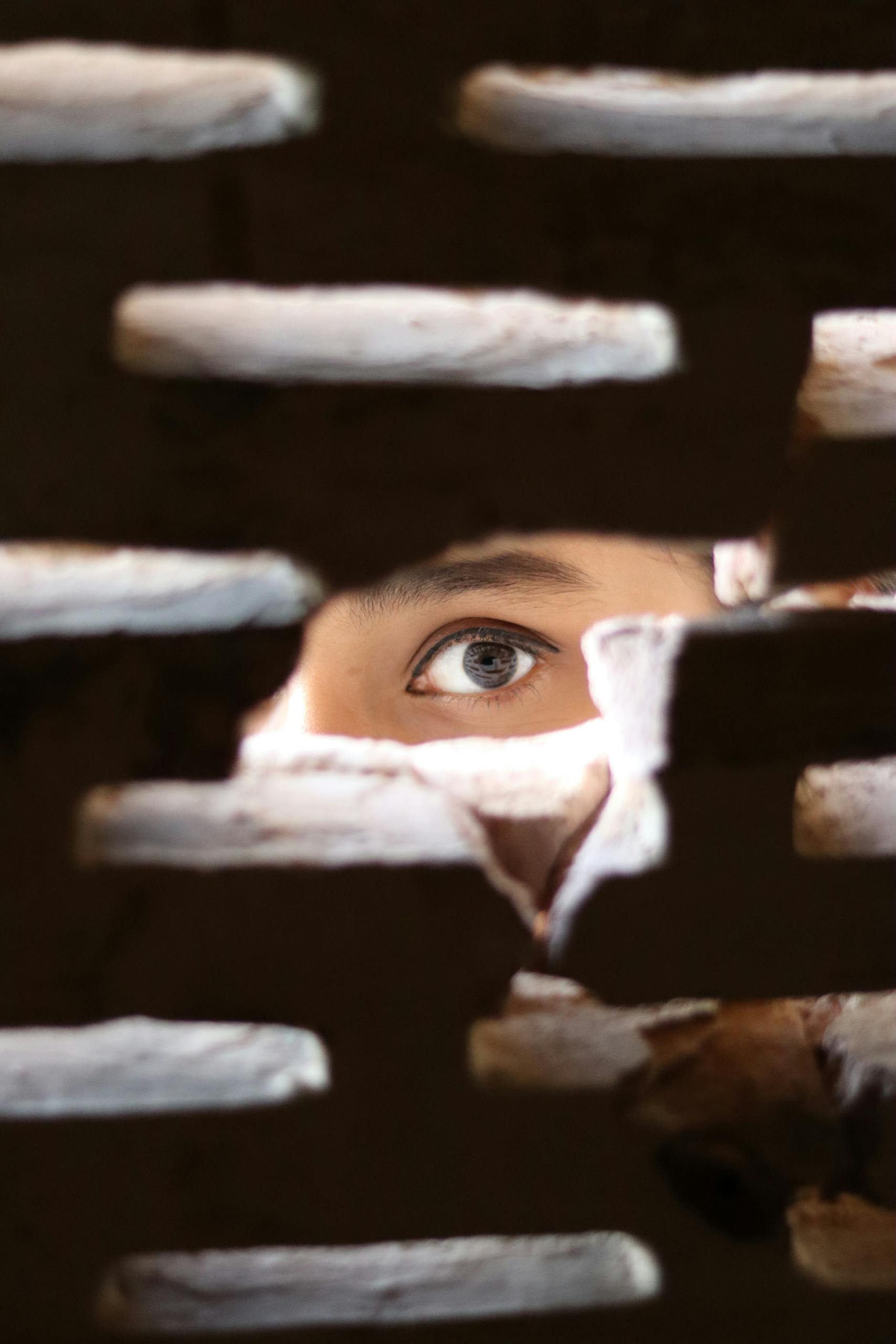 A mysterious eye peeks through a small gap in a brick wall, creating an intriguing and intense visual.